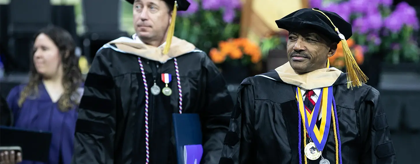 Two men in graduation robes walking down a stage.