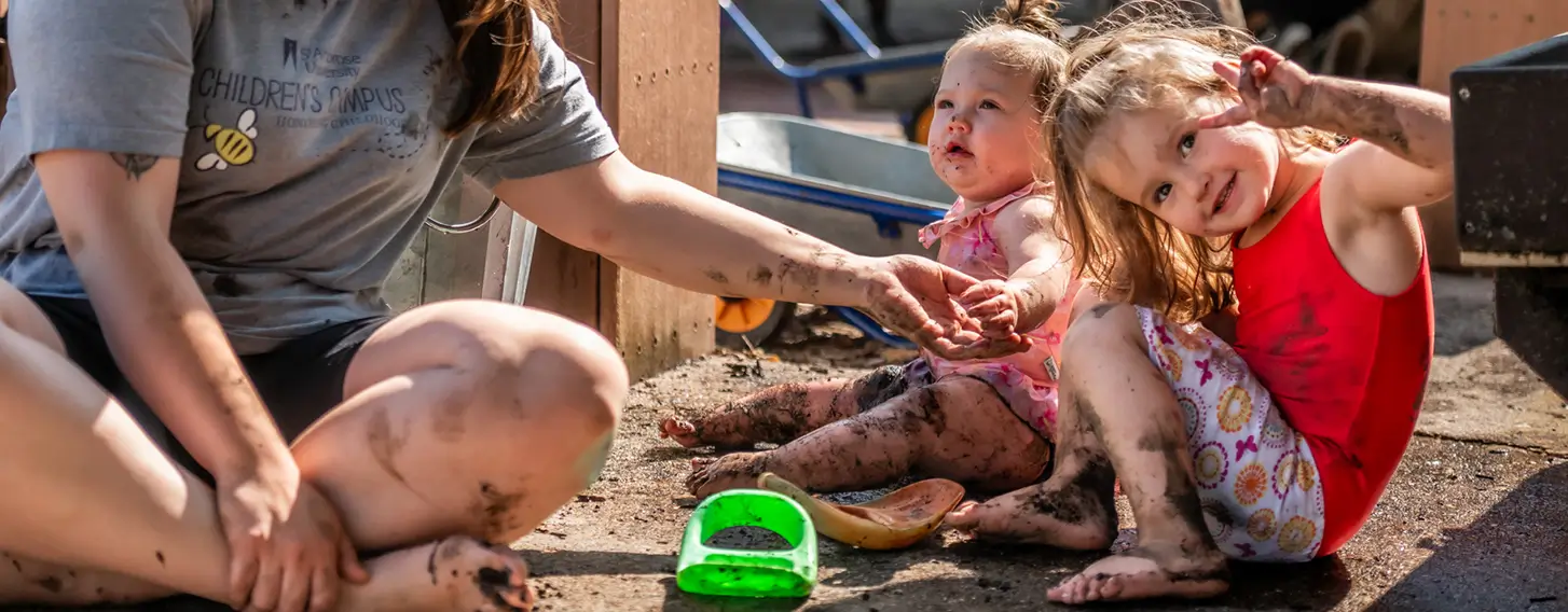 A women sitting with two young children, smiling and playing together outdoors.