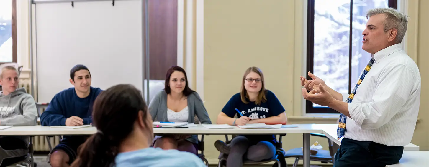 A group of students sitting around tables listening to the teacher lecture.