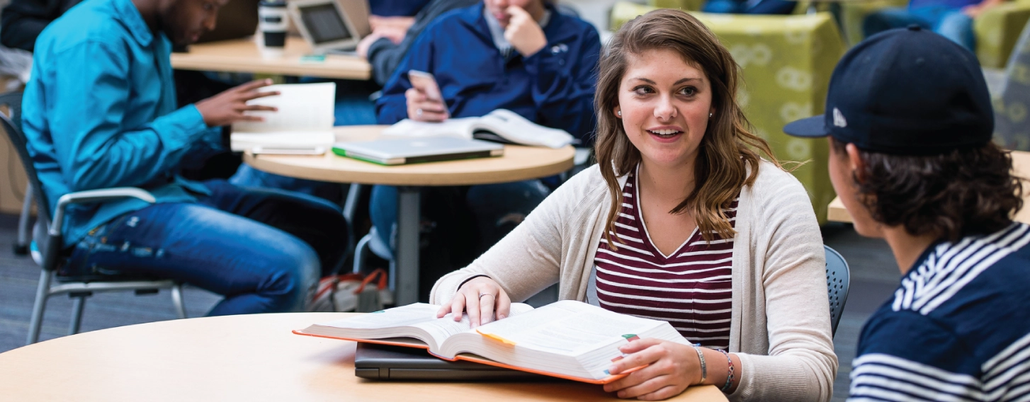 Woman discussing book with classmate.