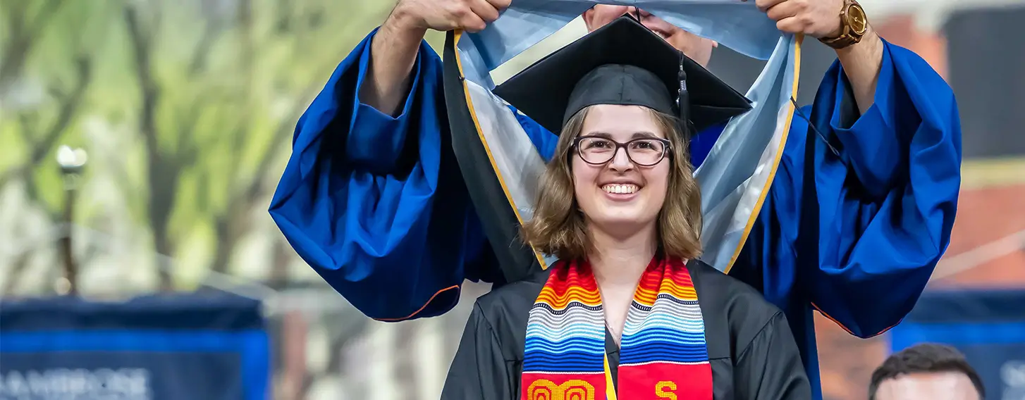 A smiling woman in a graduation cap and gown getting her masters hood.