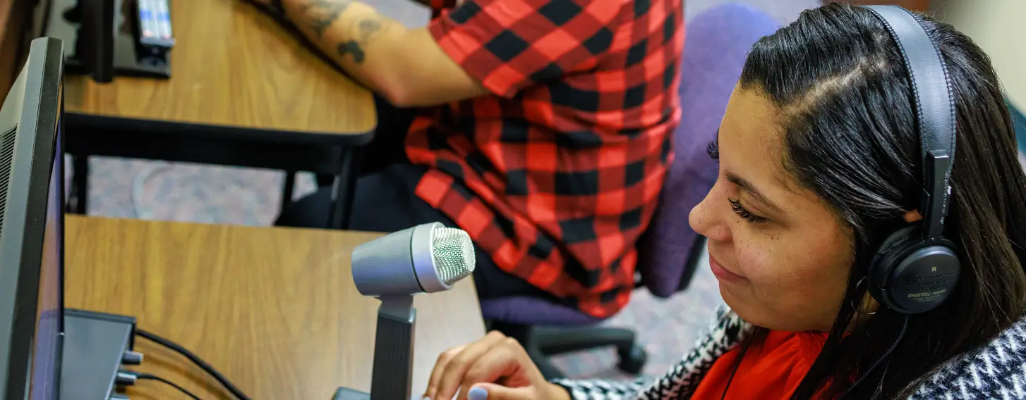 Two students wearing headphones and using microphones at desks with computers.