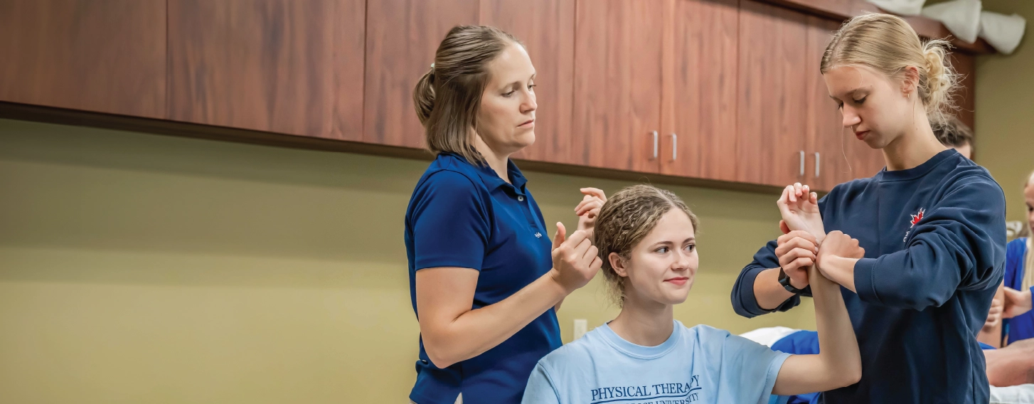 Student and teacher examining patient in physical therapy lab.