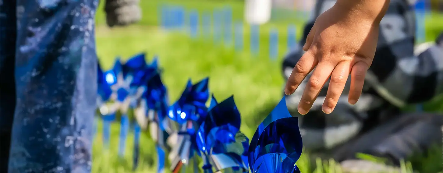 Children's hands reaching towards blue pinwheels in the grass at the Children's Campus.