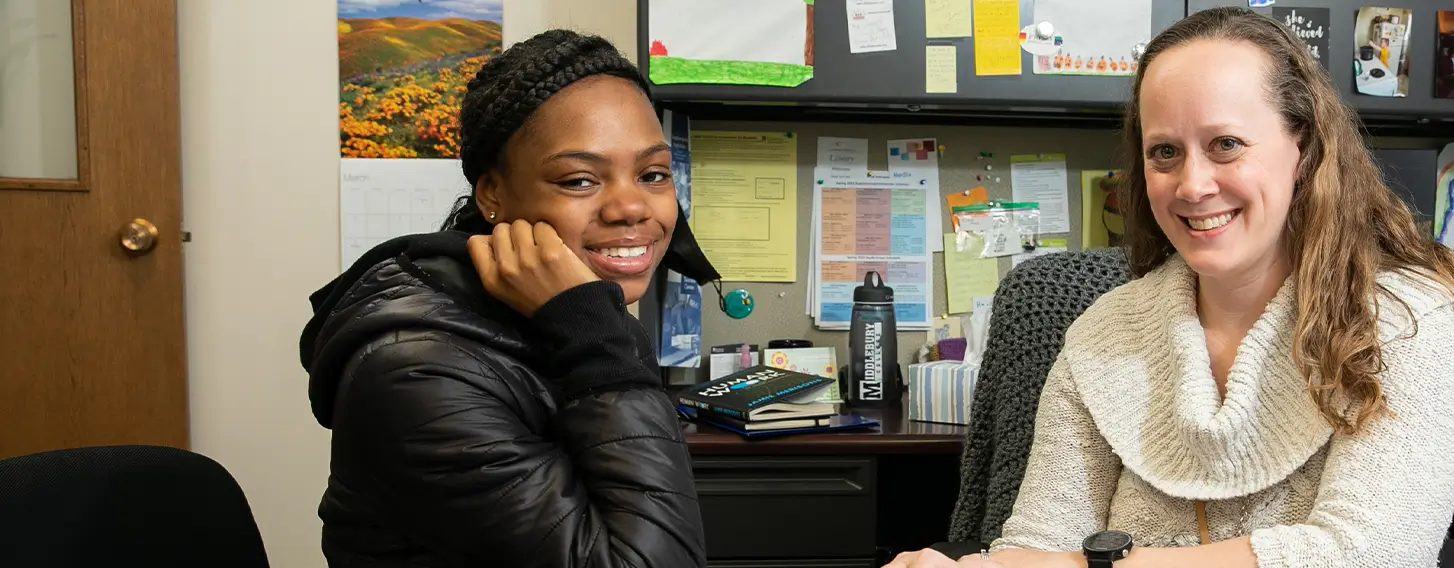 Two women sitting at a desk, looking over a folder together at Student Support.