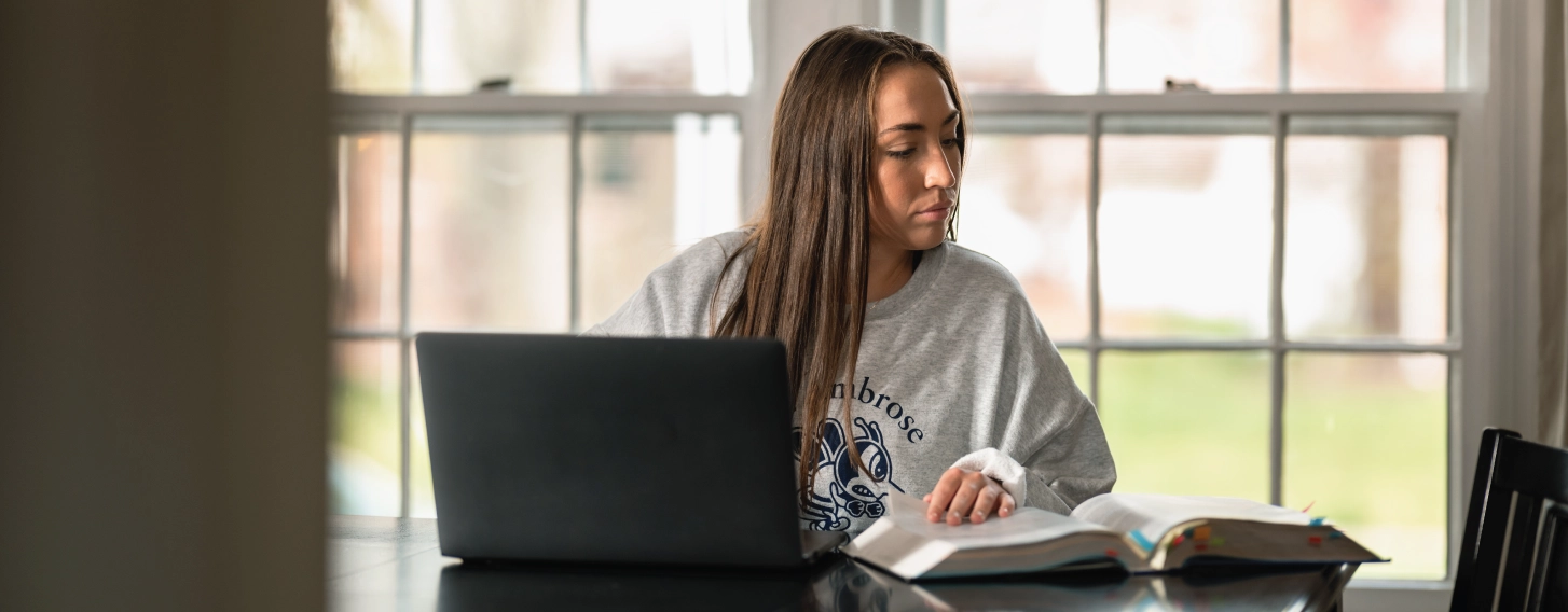 Female student on laptop during online course, referencing notes.