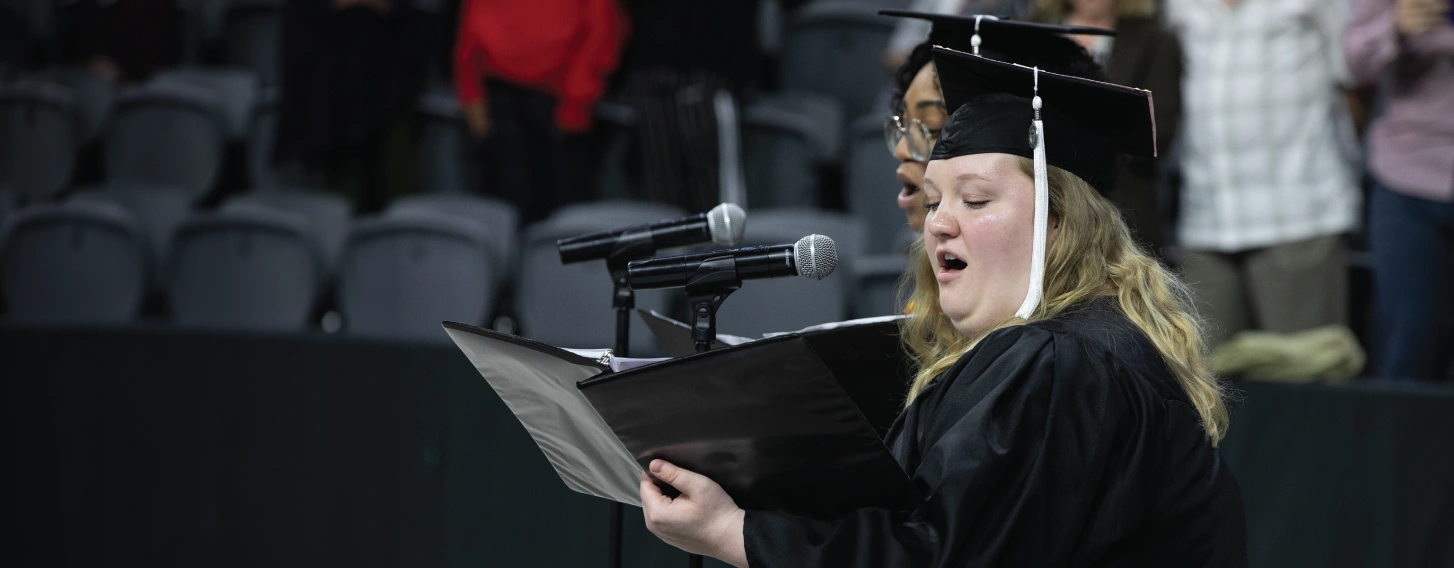 Student singing in cap and gown at graduation.