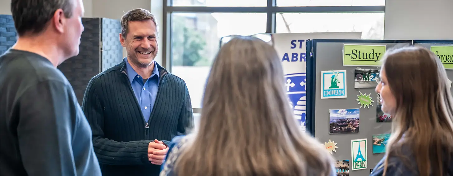 A group of individuals gthered around a posterboard for the Study Abroad program.