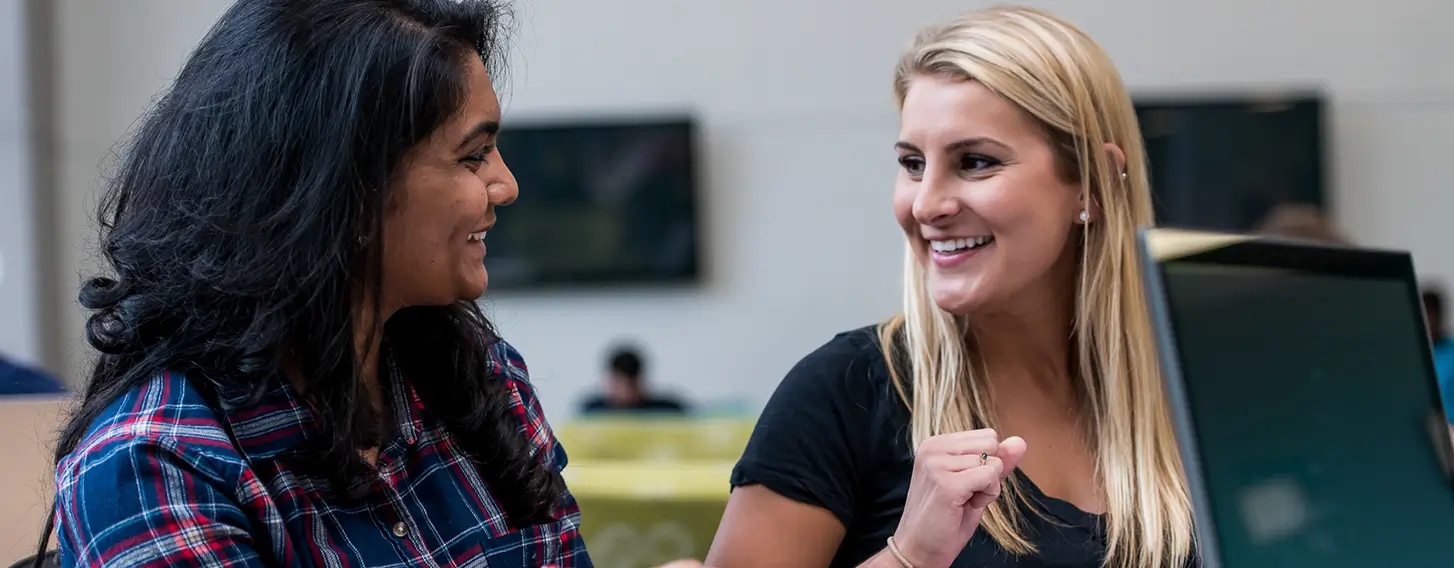 Two women sitting at a table, engaged in conversation during a beehive hangout.