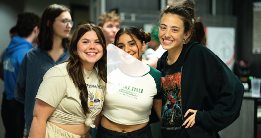 Three students posing together for a photo indoors, smiling.