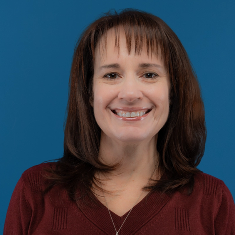 Karla Hurley smiles into the camera against a blue background.