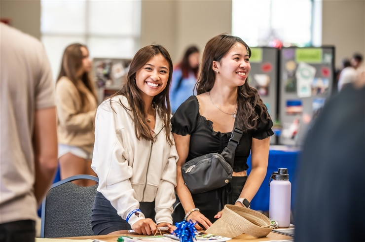 two women standing behind table at college fair