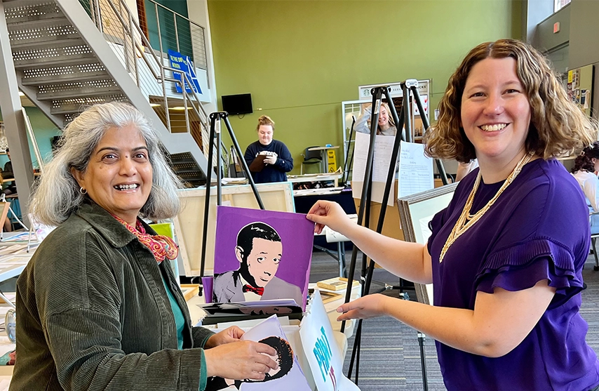 Silent Auction staff hold up artwork and smile at the camera.