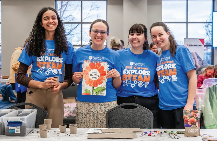 Four students smiling together wearing blue shirts that say 