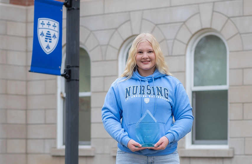 Brenna Teerlinck holds her National Blood Donation Hall of Fame award and smiles at the camera.