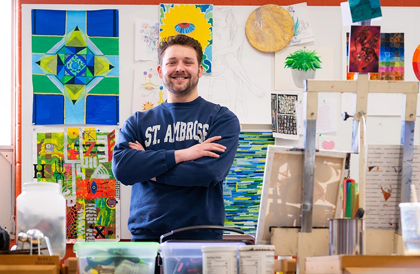 Calvin Hertel stands among canvasses, paints, and other art materials in an art studio at St. Ambrose University.