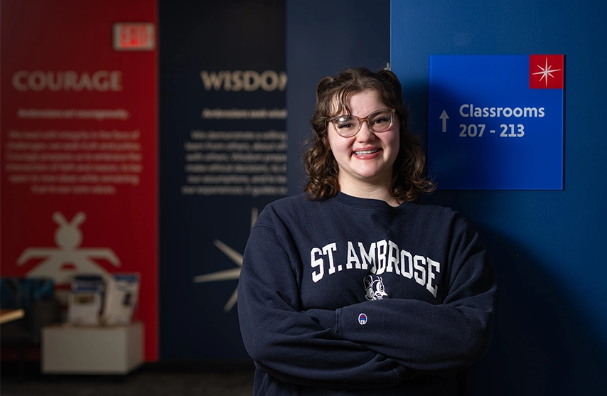 Madelyn Reum, '29, smiles into the camera against a background of the SAU values.