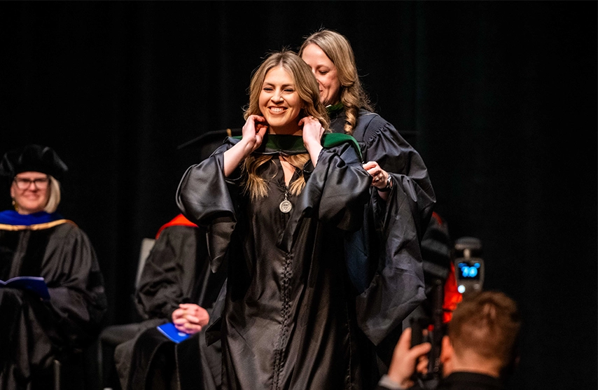 A newly graduated student from St. Ambrose University smiles as she receives her hood during the hooding ceremony.