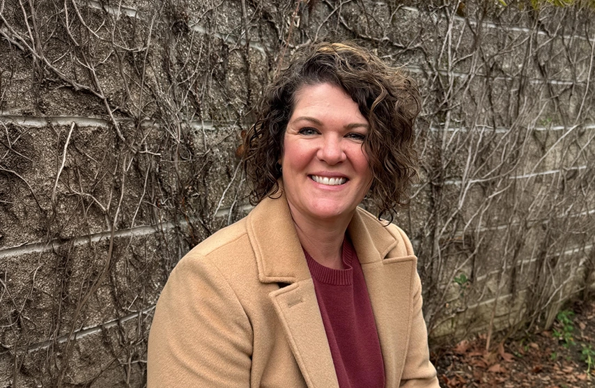 Nicole Sakraida, M.Ed, smiles into the camera against a brick background.