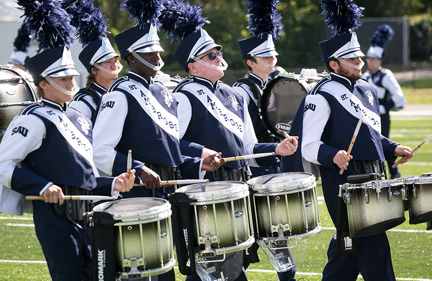 A line of drum majors drum in unison.