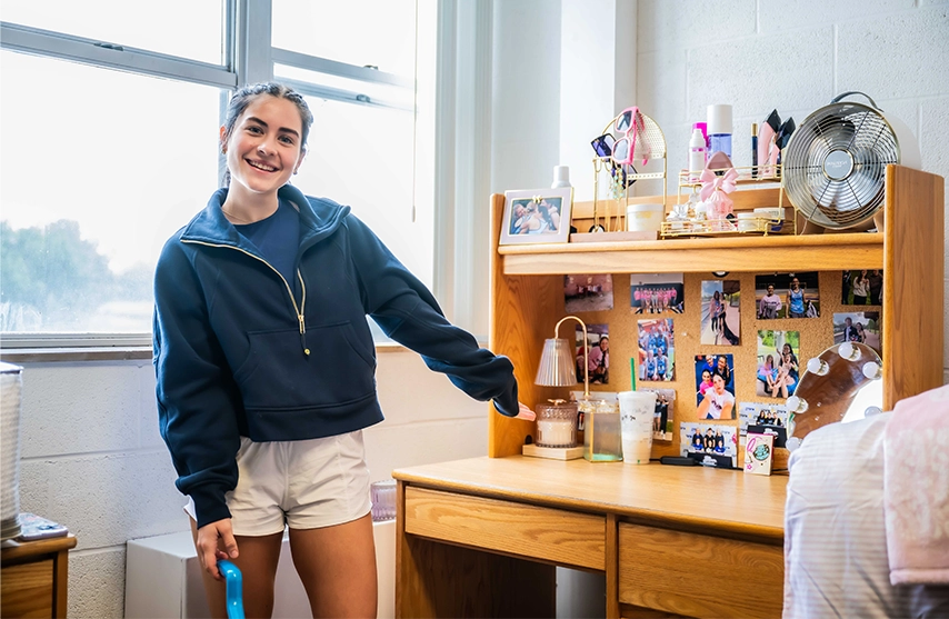 A student gestures towards her decorated desk in her SAU student housing.
