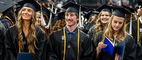 Three graduating seniors at St. Ambrose University's Commencement ceremony stand together.