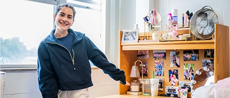 A student gestures towards her decorated desk in her SAU student housing.
