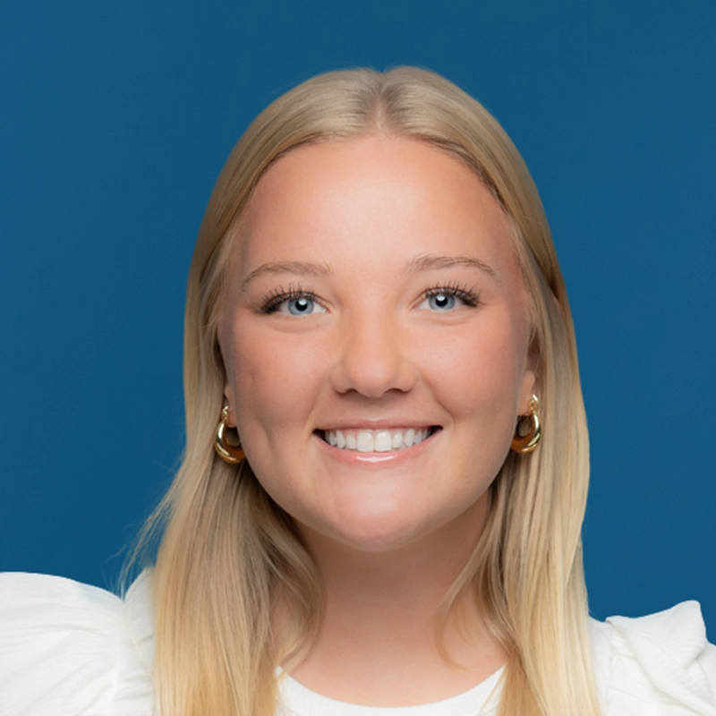 Natalie Thede smiles at the camera against a blue background.